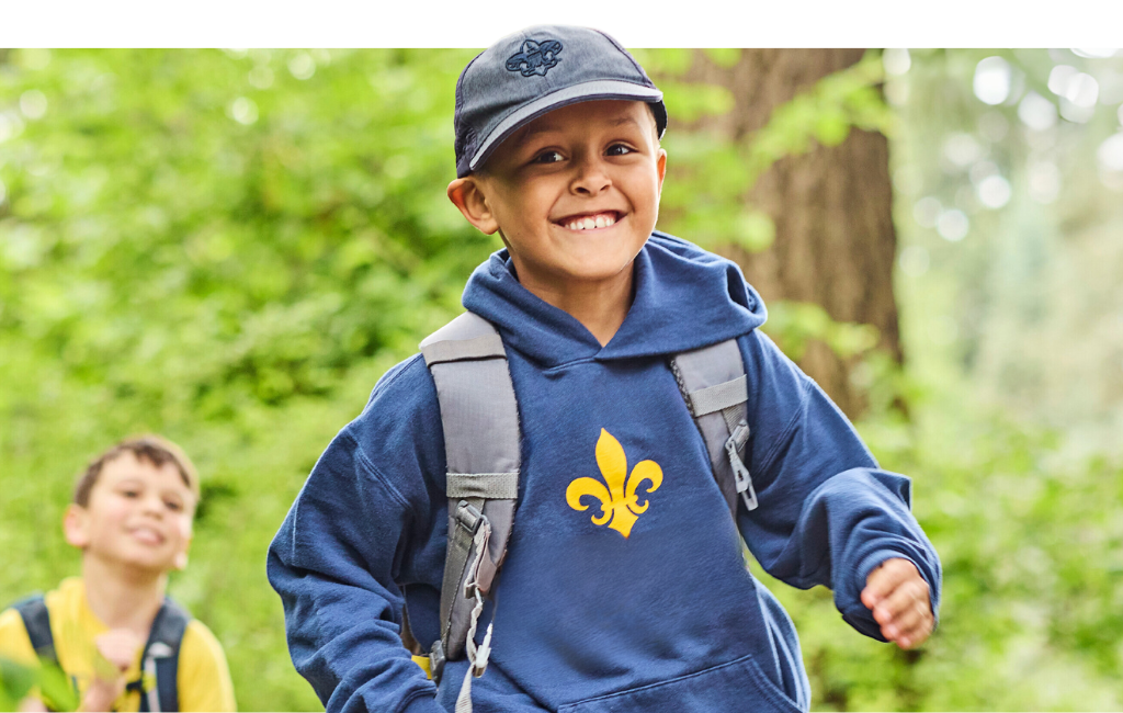 Cub Scout boy walking through forest smiling at camera.