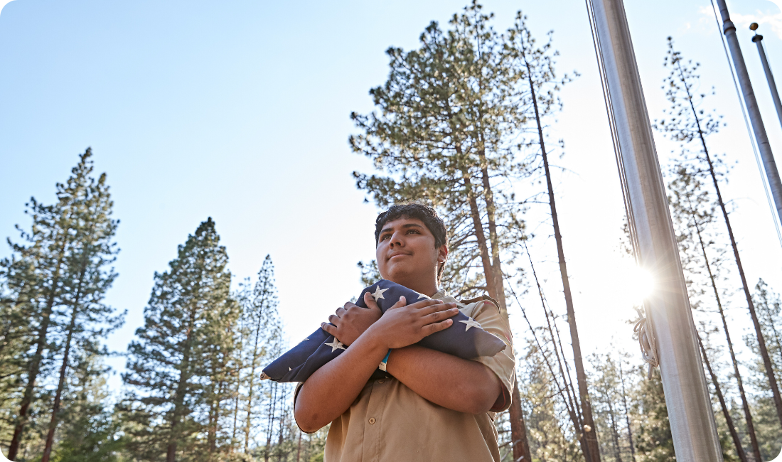 Scout BSA Boy holding folded flags in front of trees