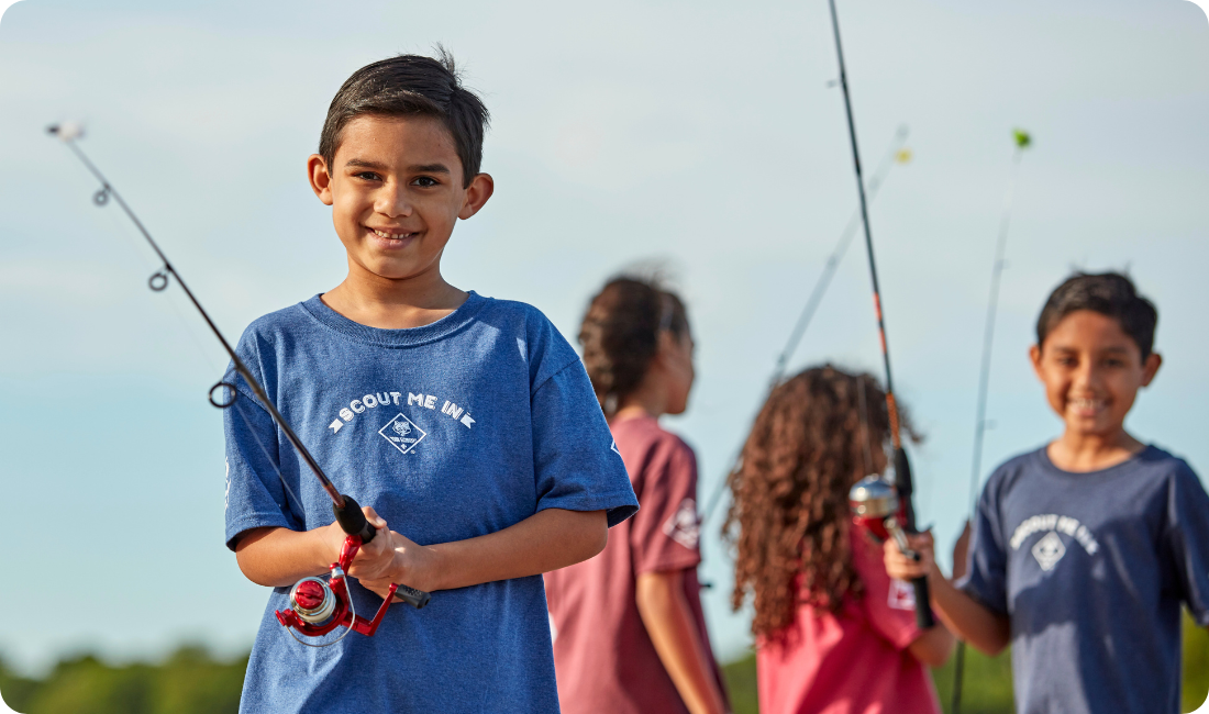 Cub Scout boy with fishing rod smiling and more scouts behind